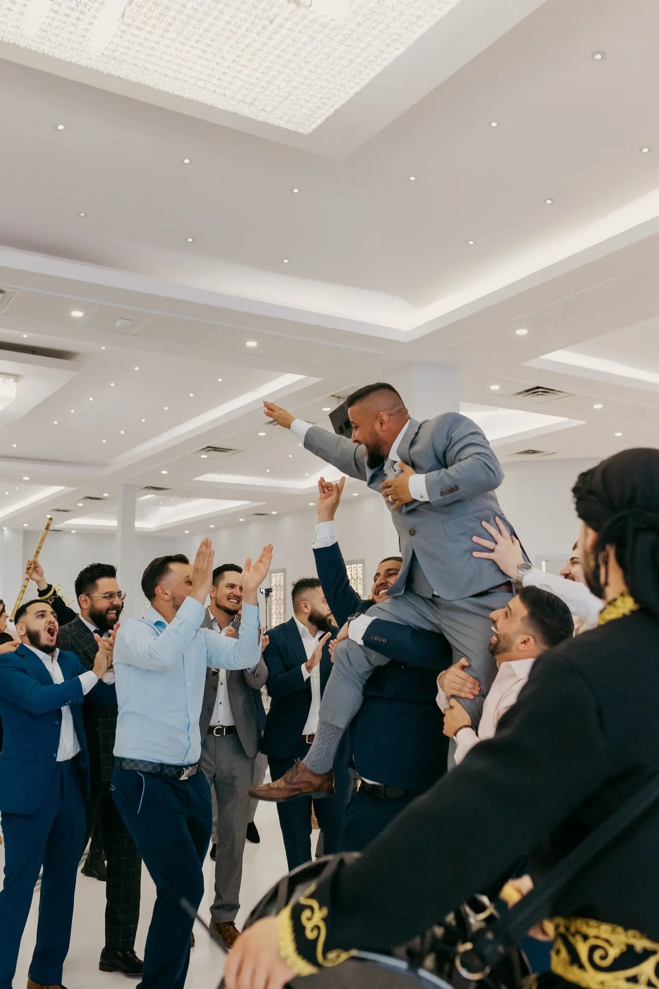 A groom hoisted on his groomsmen's shoulders in a white starlit ballroom