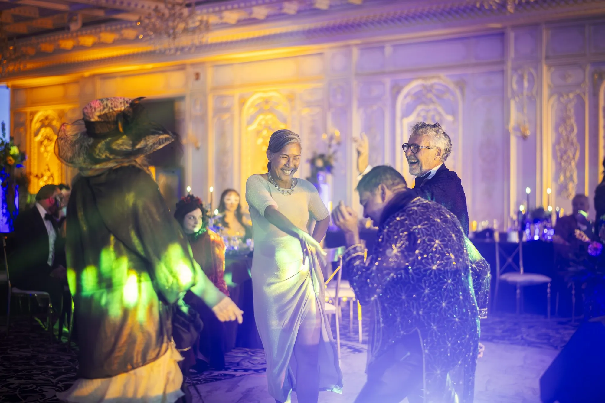 Costumed guests dancing in an ornate gilded ballroom washed in purple uplighting